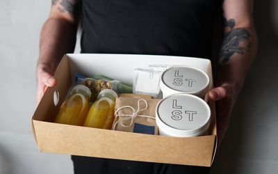 A cardboard box being held including bottles of fresh orange juice and containers of brunch food.