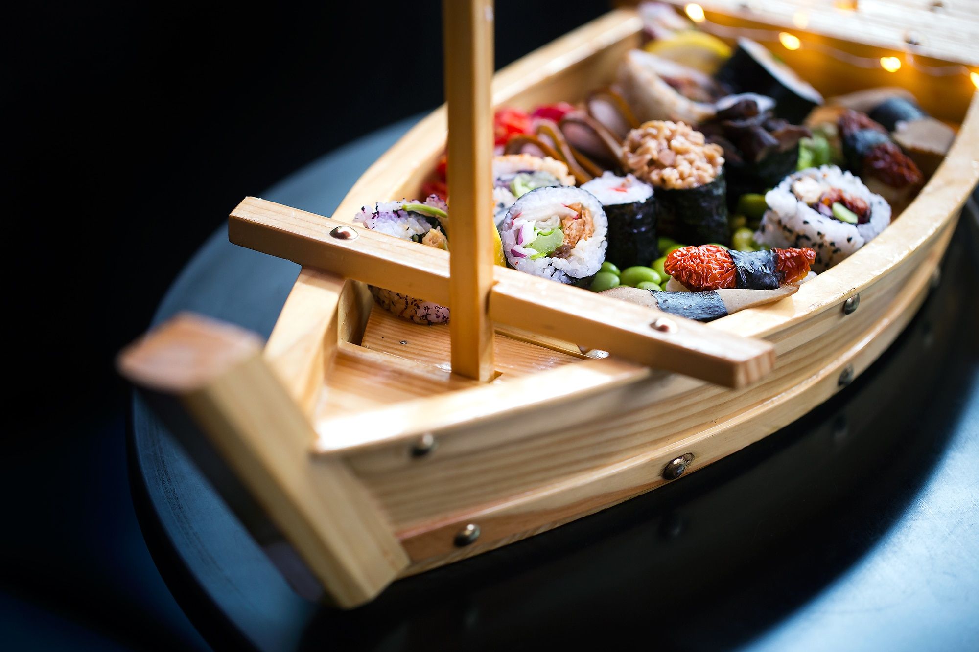 A bamboo boat filled with sushi on a dark shiny table