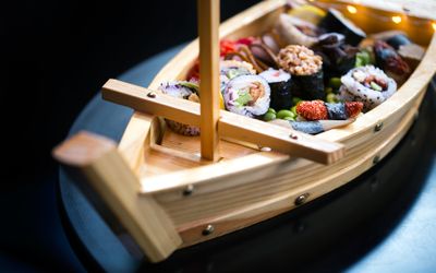A bamboo boat filled with sushi on a dark shiny table