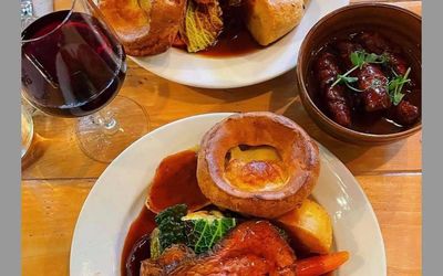 Beef roast dinners with Yorkshire puddings, a glass of red wine and gravy. Both served on white dinner plates.