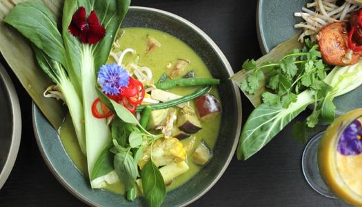 Green curry decorated with pak choi and edible flowers.