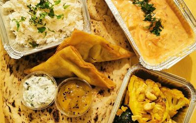 Overhead picture of takeaway curry, three foil containesrs two samosas, a naan and chutney