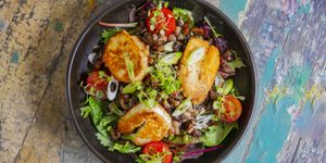 An overhead shot of a plate of halloumi and salad in a dark deep bowl on a painted distressed table