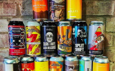 Craft ale cans piled up in front of a brick wall