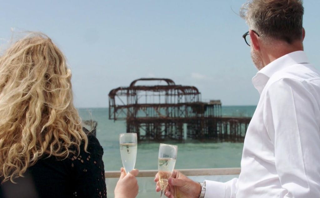 A couple drinking champagne looking out at the Brighton West Pier