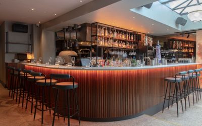 A curved wooden bar with high bar seats and an open kitchen behind.