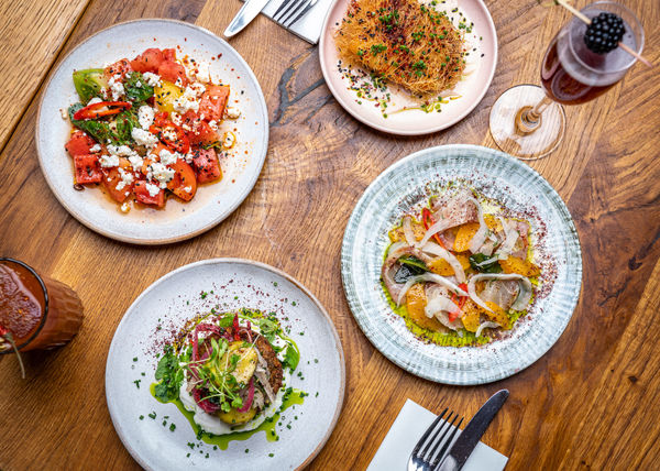 four plates of brunch shot from above with cocktails on a wooden table