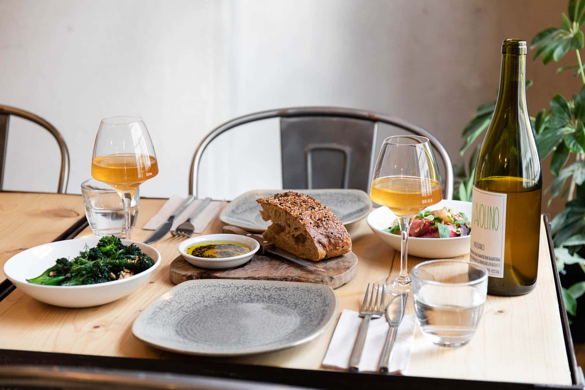 a wooden table and metal chair laid with two grey plates two glasses of orange wine and a selection of small plates