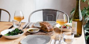 a wooden table and metal chair laid with two grey plates two glasses of orange wine and a selection of small plates