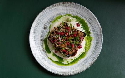 One of the dishes at Best restaurant Brighton winner Burnt Orange. Miso Aubergine Crispy Onions, Sour Cream and Pomegranate. Smoky, vegan. Bright green dressing and bright red pomegranate seeds stand out on a simple plate. Place to eat in Brighton