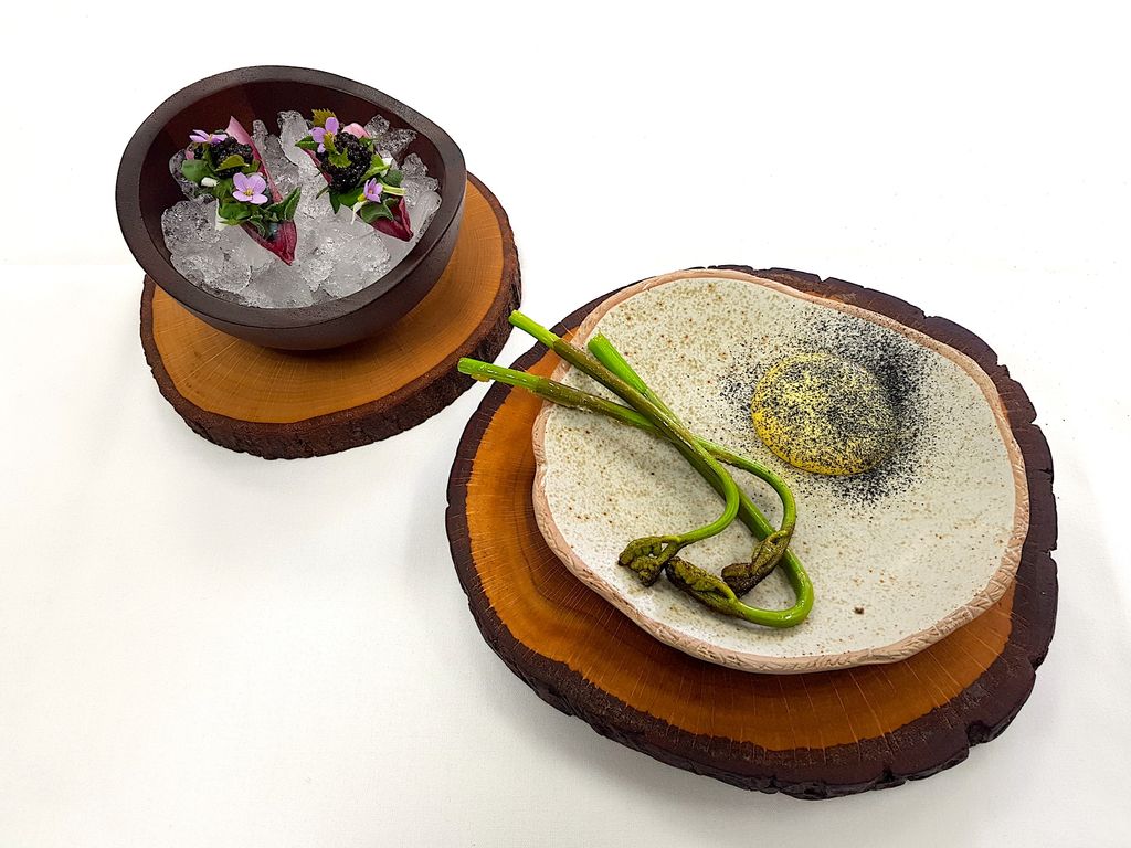 two small plates of foraged food presented on a white tablecloth and wooden disks