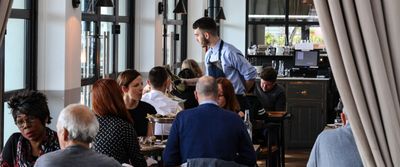 A member of staff serving food in the busy restaurant The Salt Room during daytime service with the sun shining through the windows.