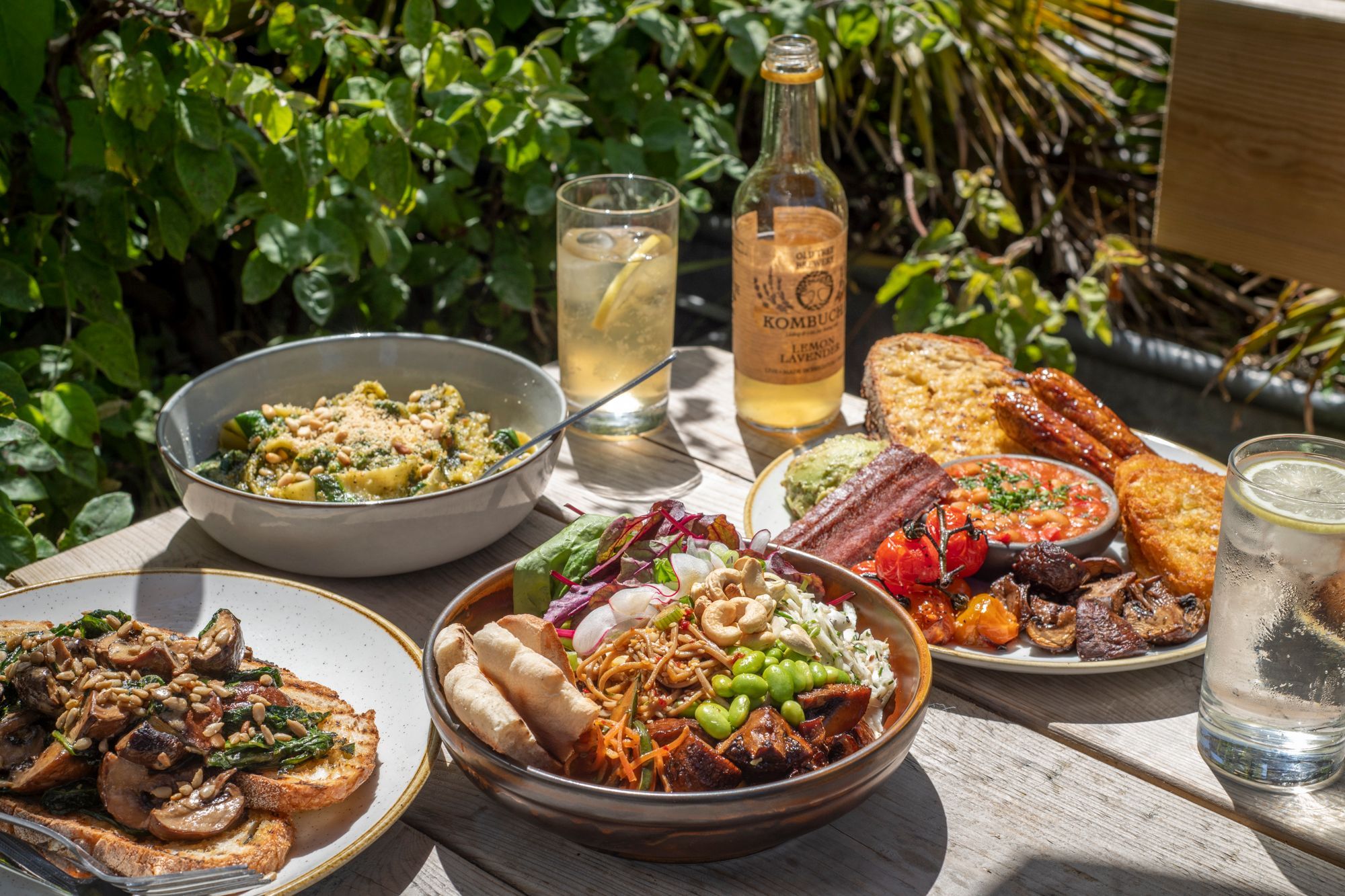 outdoor table laid out with four different dishes including buddha bowl, enlighs breakfast, mushrooms on toast