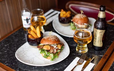 table laid out with two burgers with chips on side and two beers