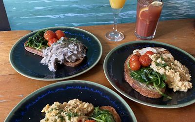 Plates of brunch with roasted cherry tomatoes, spinach and scrambled egg. Served with a glass of mimosa and Bloody Mary.