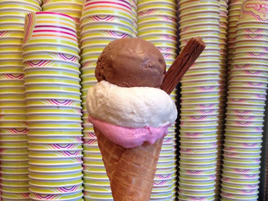 a waffle ice cream cone containing a pink, white and brown scoop of ice cream and a flake