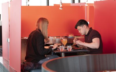Romantic Restaurants Brighton Guide. a romantic couple sat opposite each other. Sat in a pod at Moshimo, with a black table and red dividers.