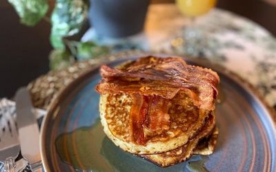 A blue plate with a stack of pancakes, crispy bacon and maple syrup