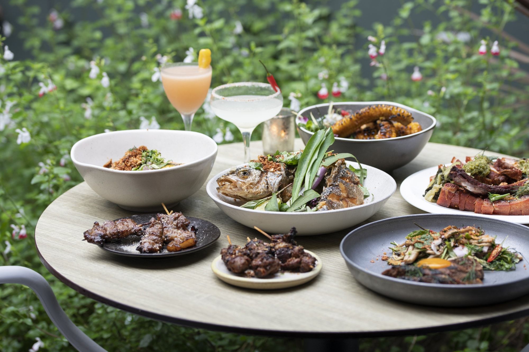a selection of Lucky Khao Brighton dishes situated on a table in their rear garden. BBQ skewers, grilled fish, corn ribs, a mouthwatering selection. 