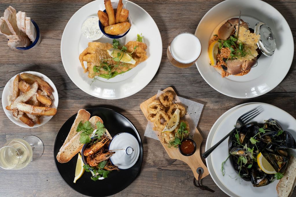 table laid with four different dishes including fish and chips, mussels, prawns, lobster and onion rings as side dish