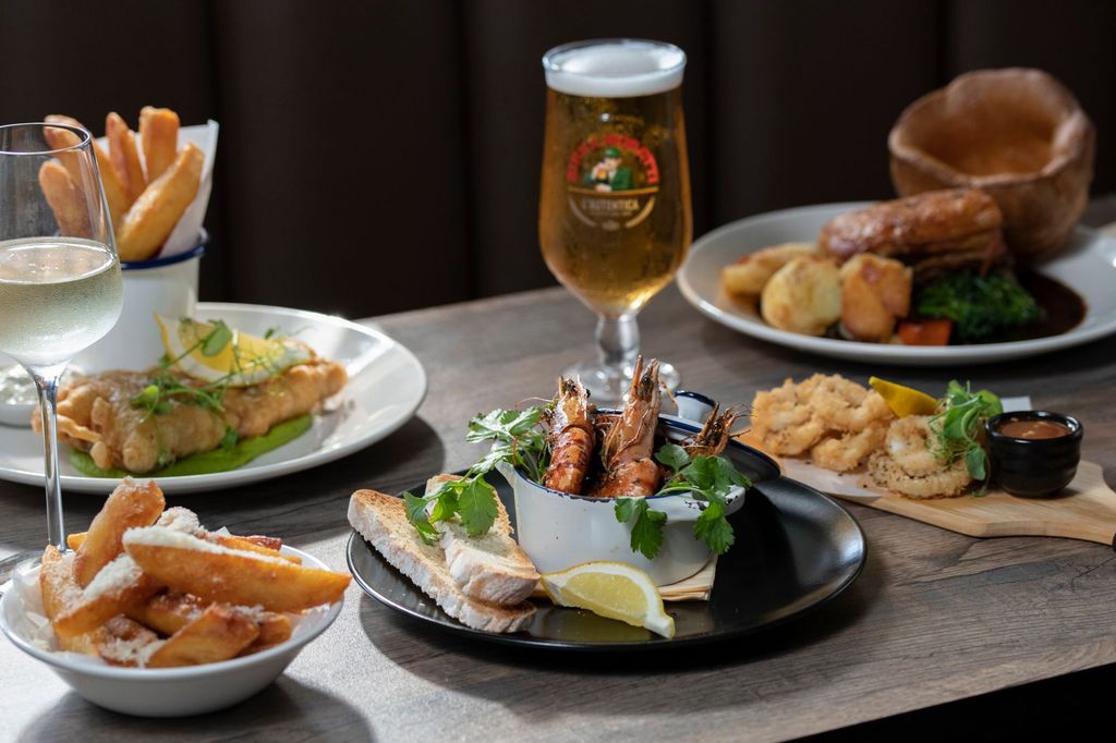 table laid out with few dishes but camera focuse on prawns with chips and bread, beer served as a drink