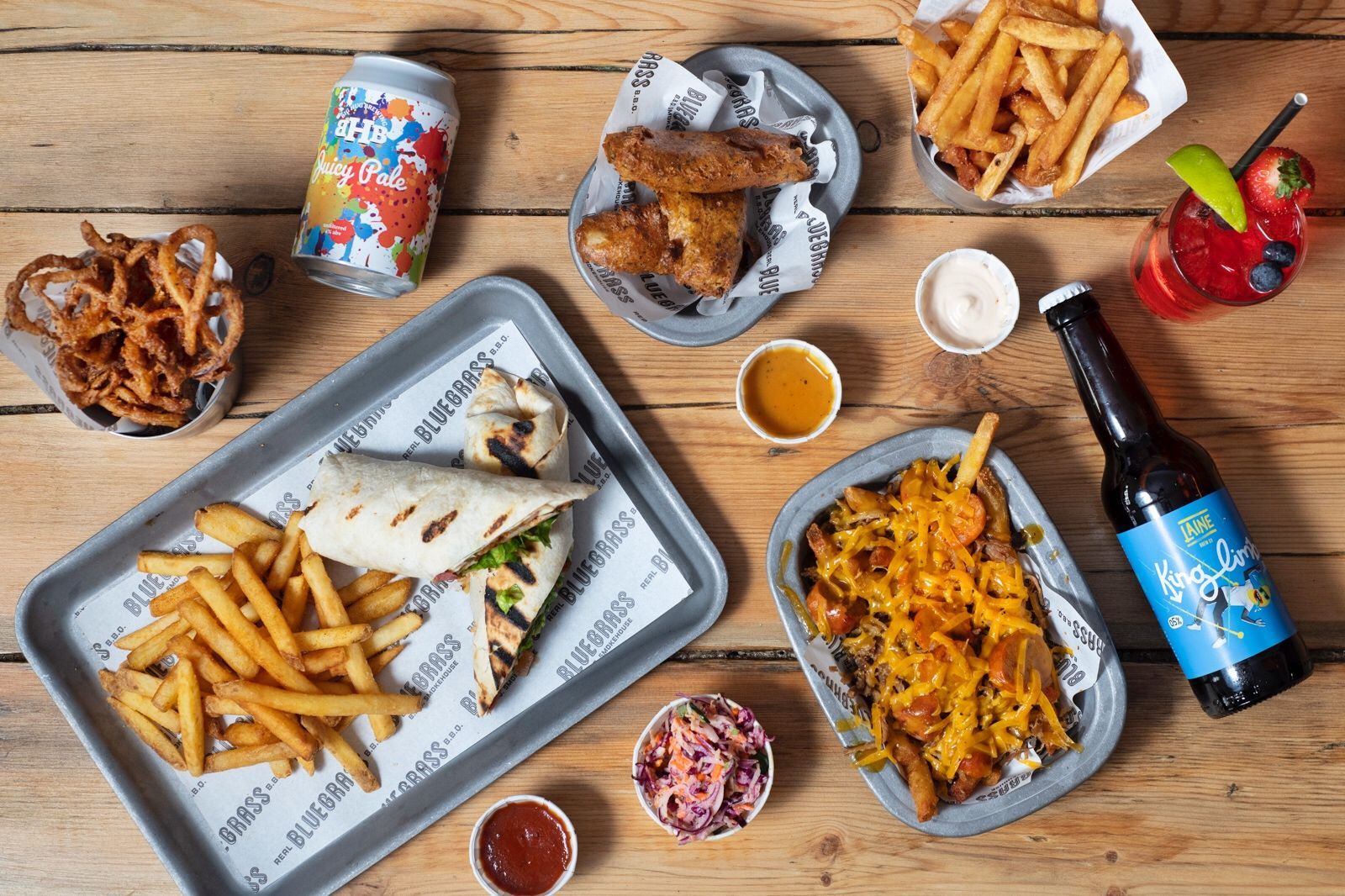 table laid out with food and drink including wrap and fries,beer, cocktail, sauce