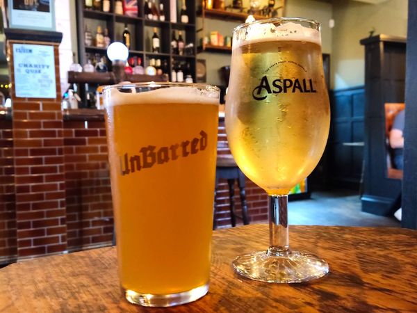 A pint of Unbarred beer and a pint of Aspals cider on a wooden table in a pub. Pub Dinner