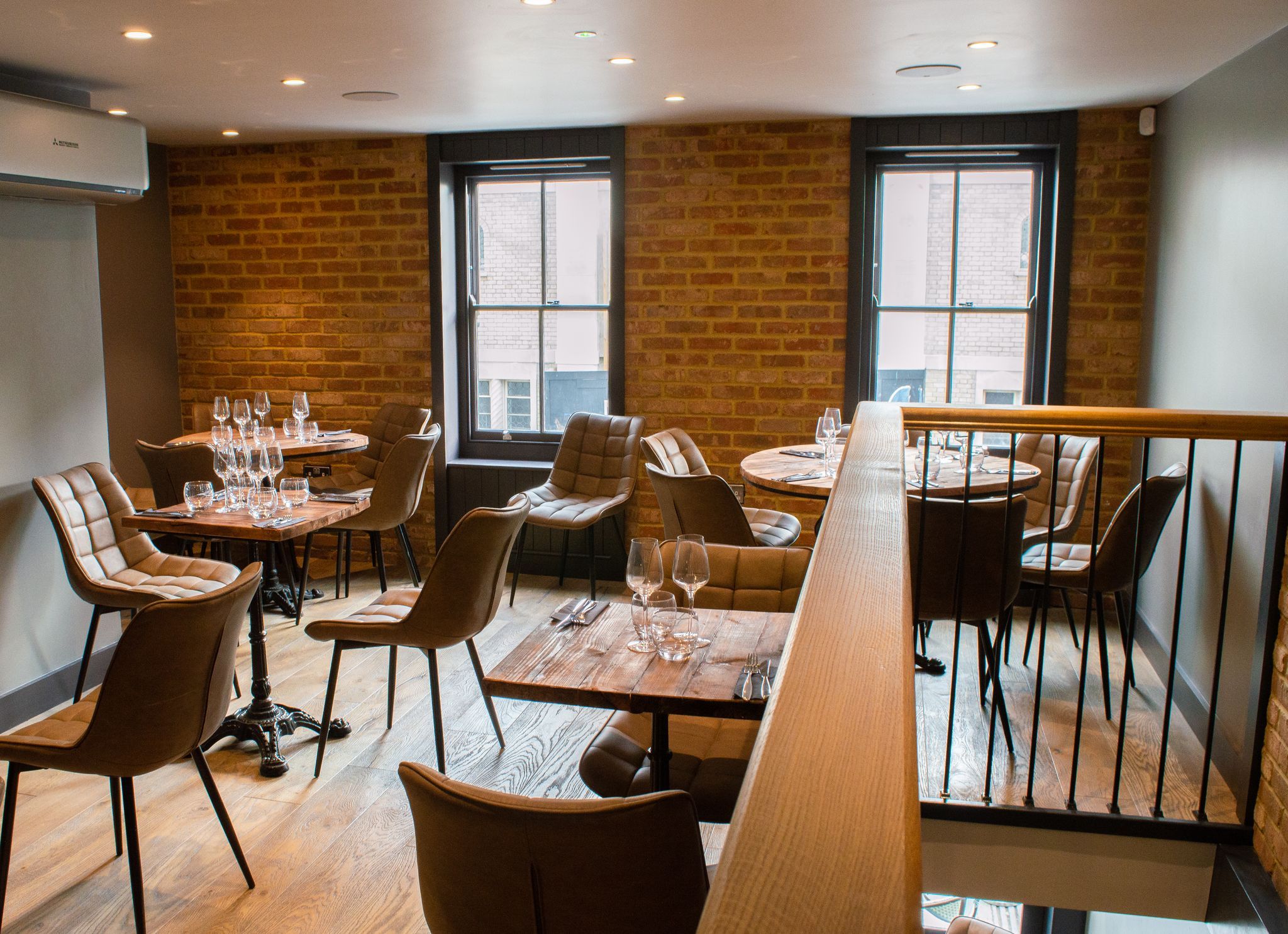 Upstairs At TEN Brighton. A redbrick wall looks out onto a street, wooden tables set with tableware and deep brown leather seats