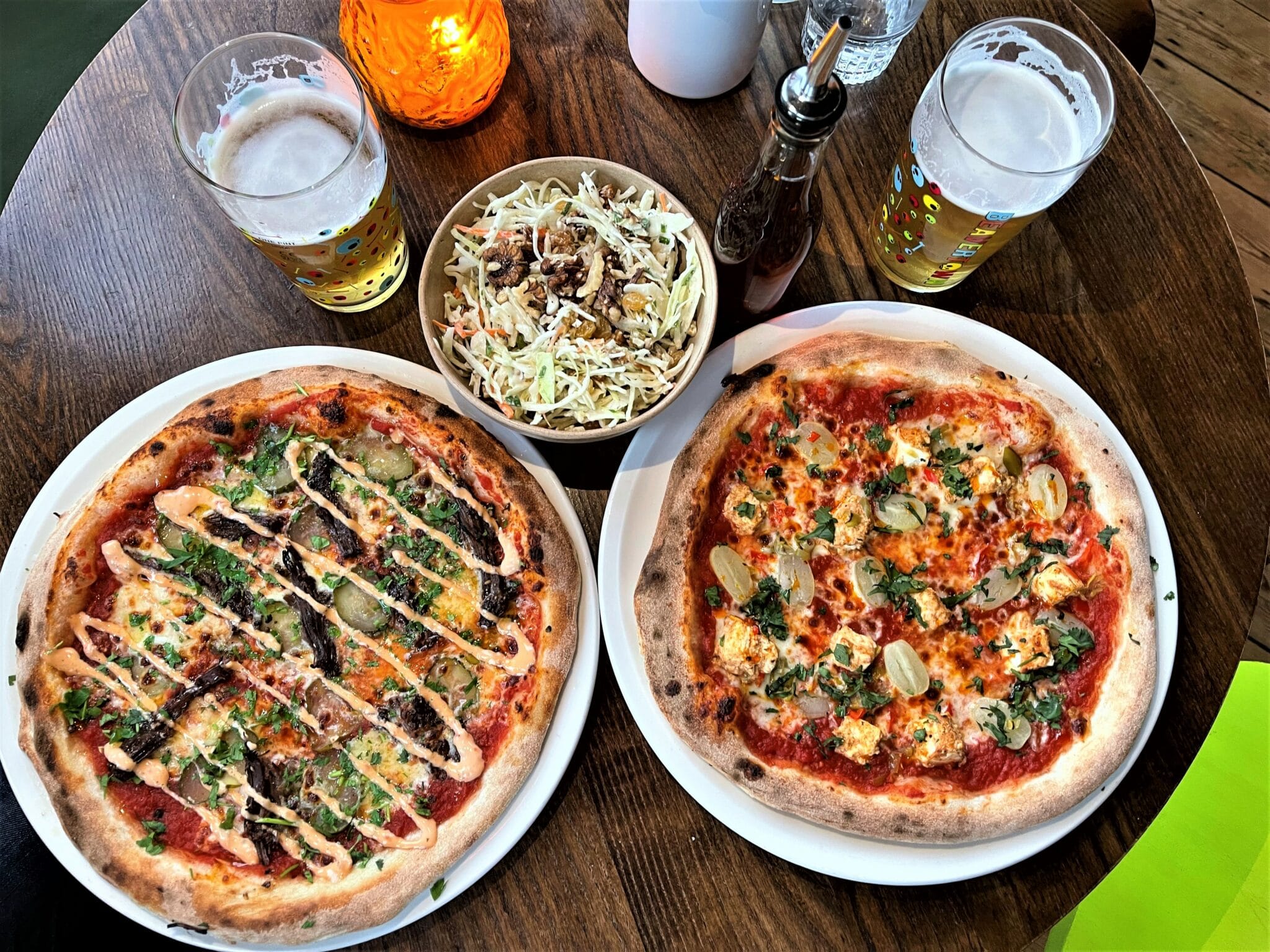 table laid out with two different types of pizzas two glasses of beer