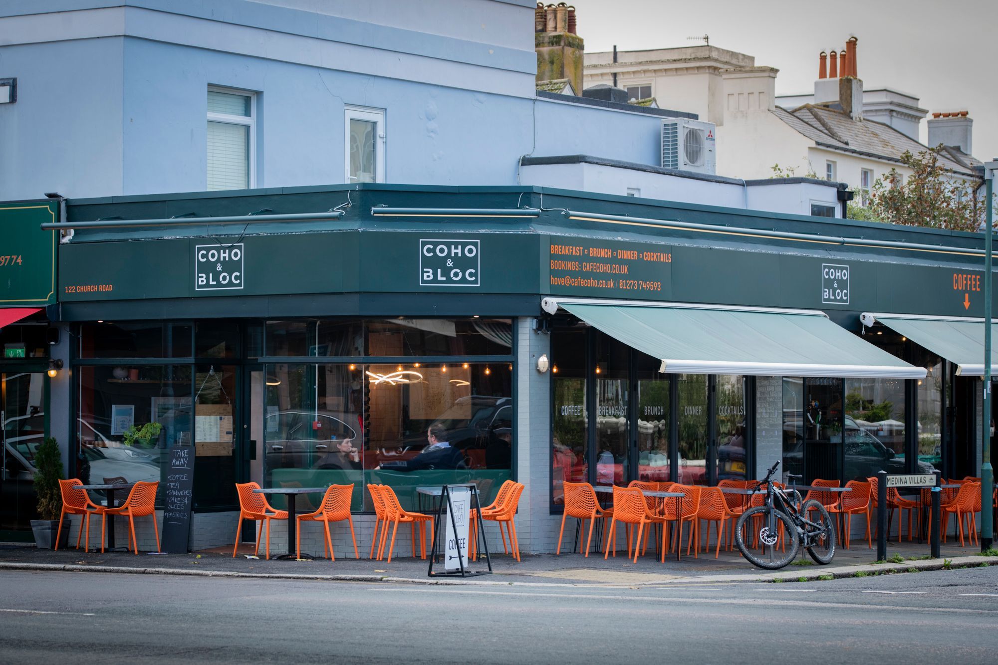 exterior of cafe coho in hove, outside seating area with dark coloured tables and orange chairs