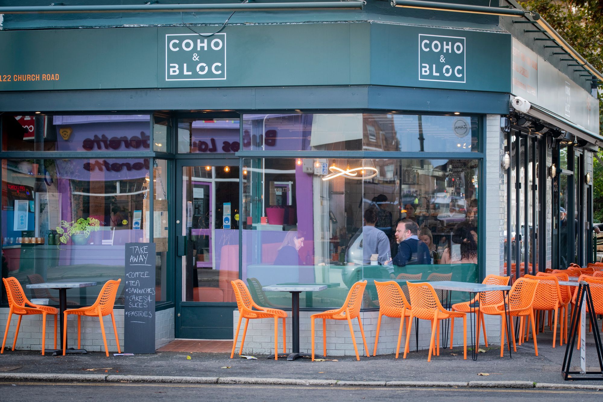exterior of cafe coho in hove, outside seating area with dark coloured tables and orange chairs