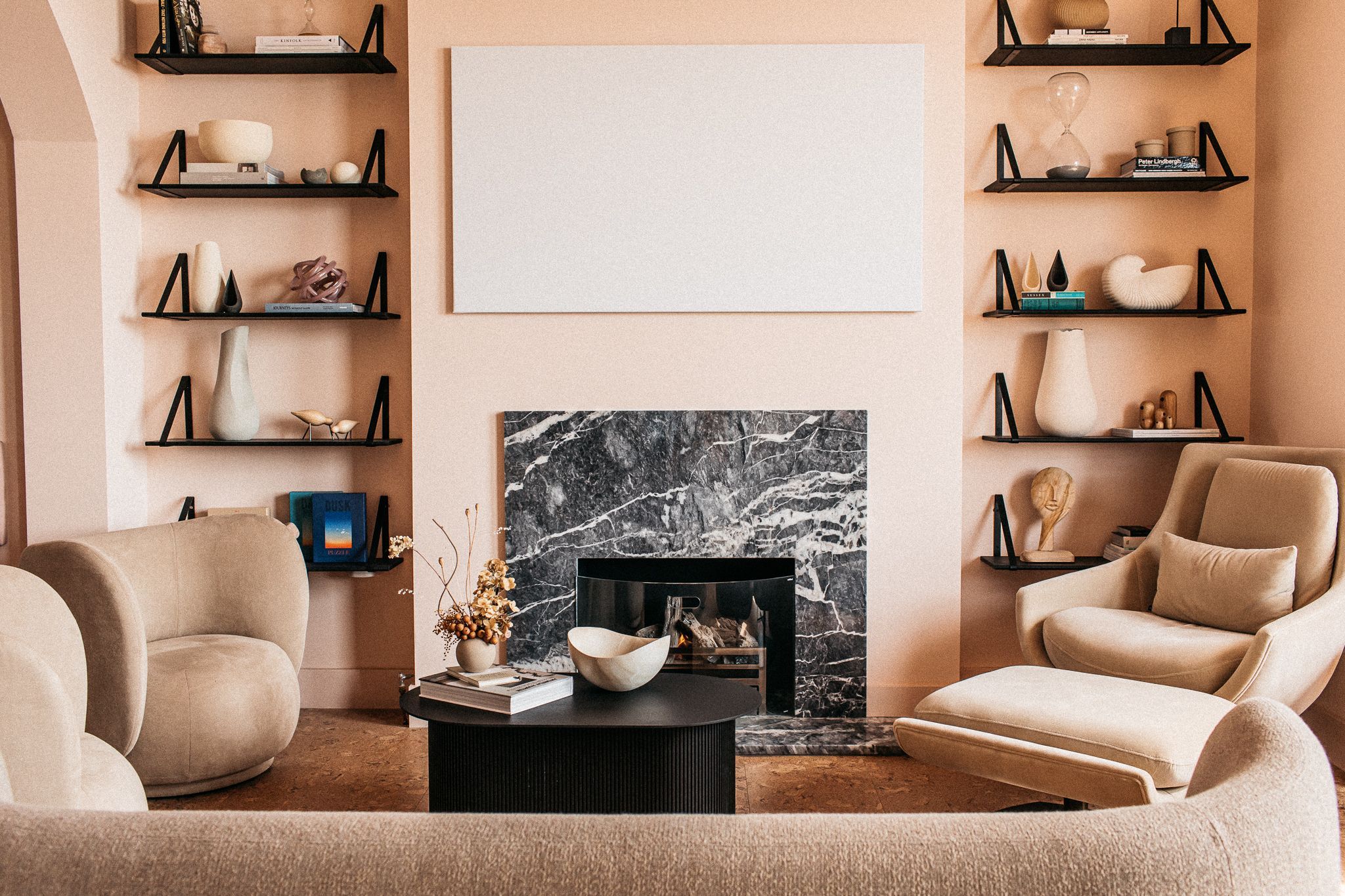 cosy sitting area with beige painted walls, comfy beige sofas, small black tables and shelves with diffrent decorations