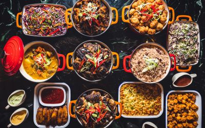 Overhead shot of cast iron pots of food, coleslaw, rice and peas, chicken, curry, plantain