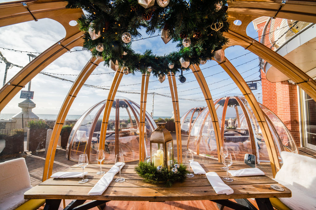 Brighton igloo at Shelter Hall on Brighton seafront. In foreground a wooden table laid for dinner with cutlery and napkins. A perfect option for Valentines Day Brighton