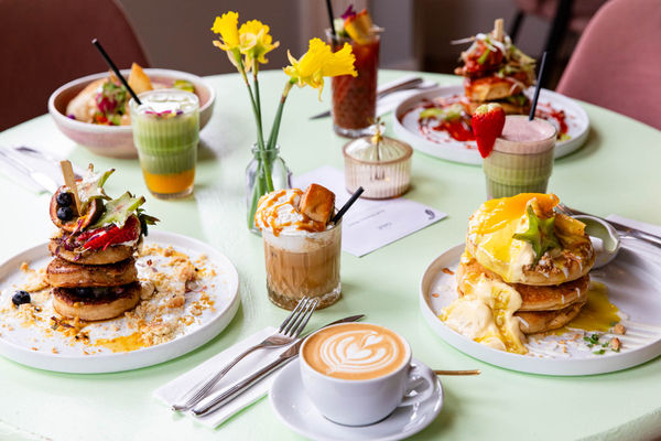 side shot of the light green table laid out with four brunch dishes including frumpets, eggs on the toast, veggie bowl, coffes and smoothes