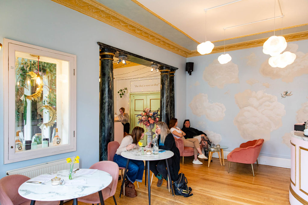 Interior shot of the lovely and warm Oeuf cafe, people sitting on the light pink chairs and talking and eating, light blue walls decorated with clousds