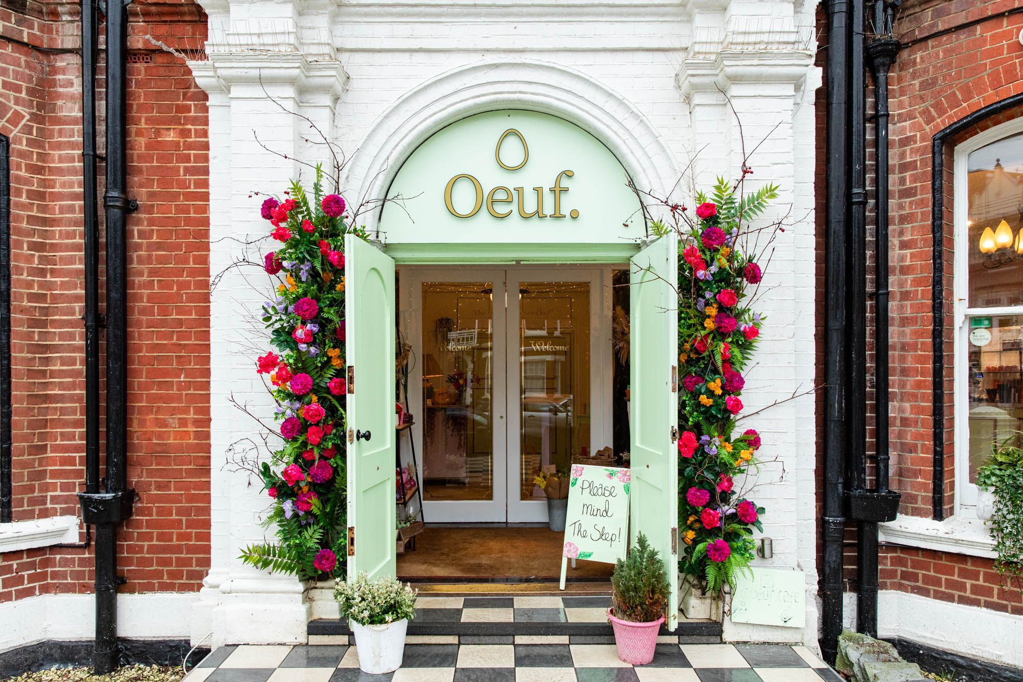 exterior shot of the Oeuf cafe. Light green entrance door decorated with lovely colourful flowers.