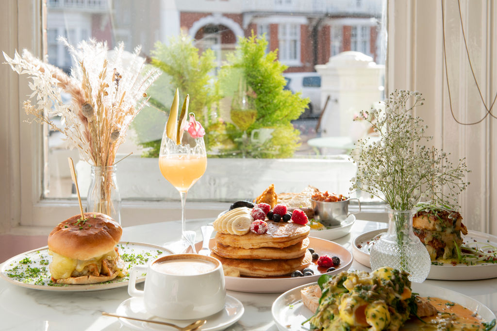A table by a window laid with brunch, including coffee mimosa, pancakes and burgers