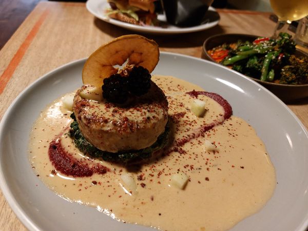 A medallion of celeriac with berries and an apple crisp on top in a creamy peppercorn sauce and a streak of beetroot puree
