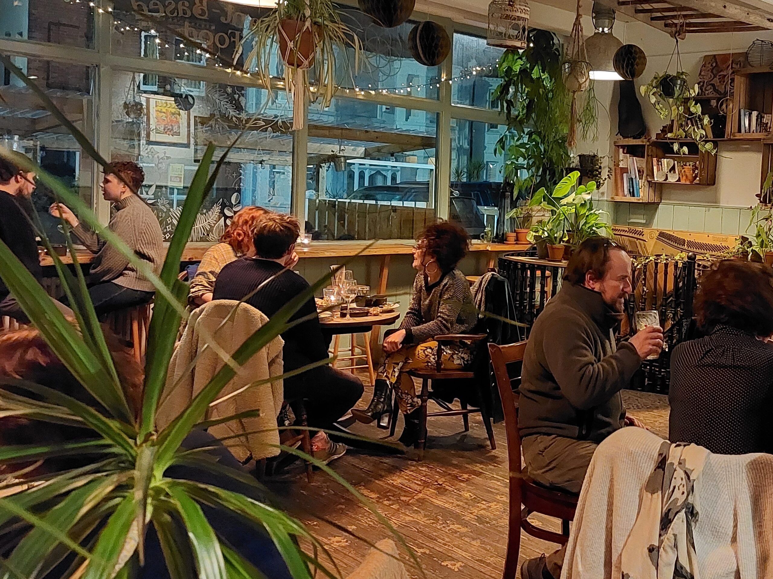 wooden floors and tables, leafy plants and people sat at tables eating and drinking
