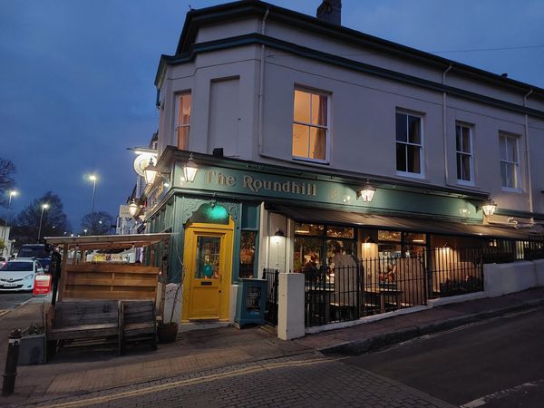 A pub on a corner of a street with a yellow door and green exterior, twilight outside and light on in the pub