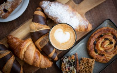 pastry and coffee placed on wooden board, on wooden counter top. Brighton takeaway service on these items is available