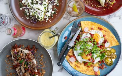 The bottomless brunch at BAKED. A plate of food showcasing huevos rancheros, cutlery placed on the blue plate, with a side of pickles and parsley to garnish