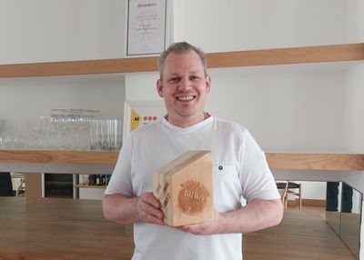 A smiling man in Chef's whites holds up a wooden BRAVO trophy