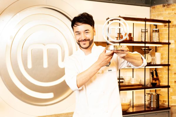 A man with dark hair in chef whites is holding up a MasterChef trophy