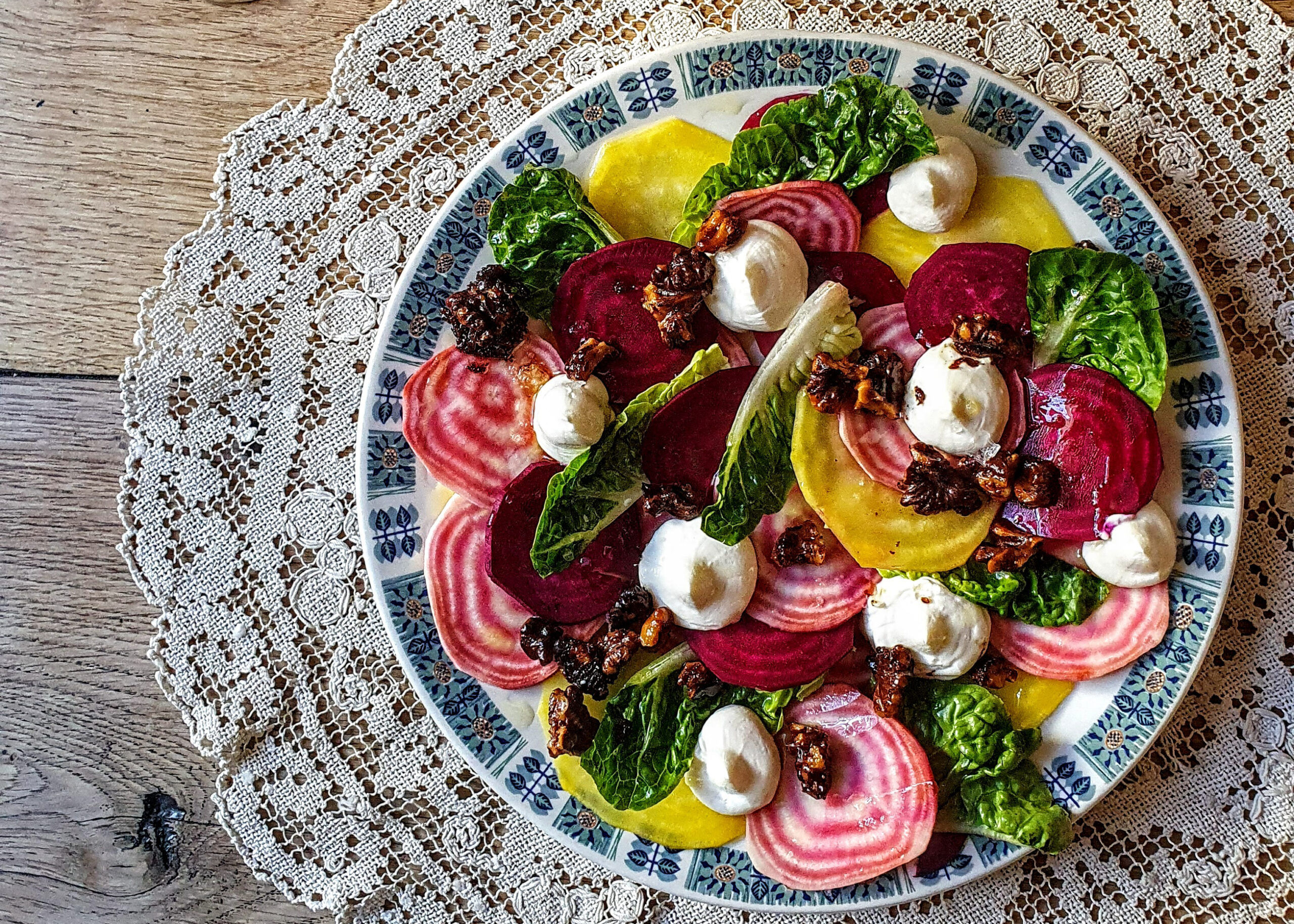 A colourful plate of sliced radishes, beetroot and cheese served on a plate which sits on a lace doily. 