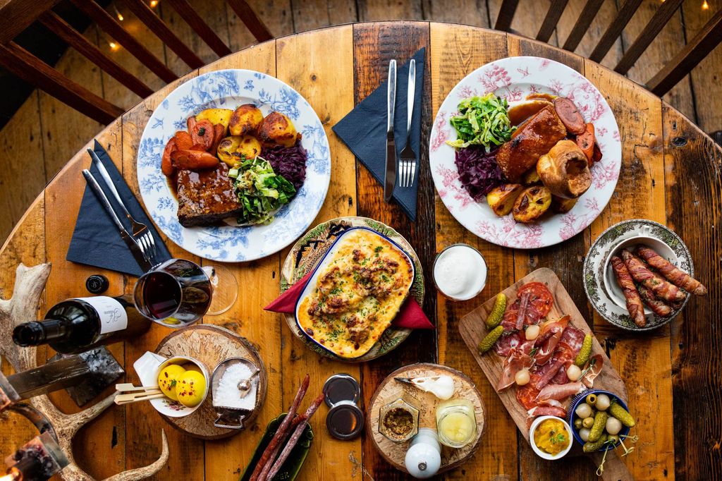 The Farm Tavern wooden tabled filled with Sunday lunch dishes including Sunday roast, British pie, wine and beer