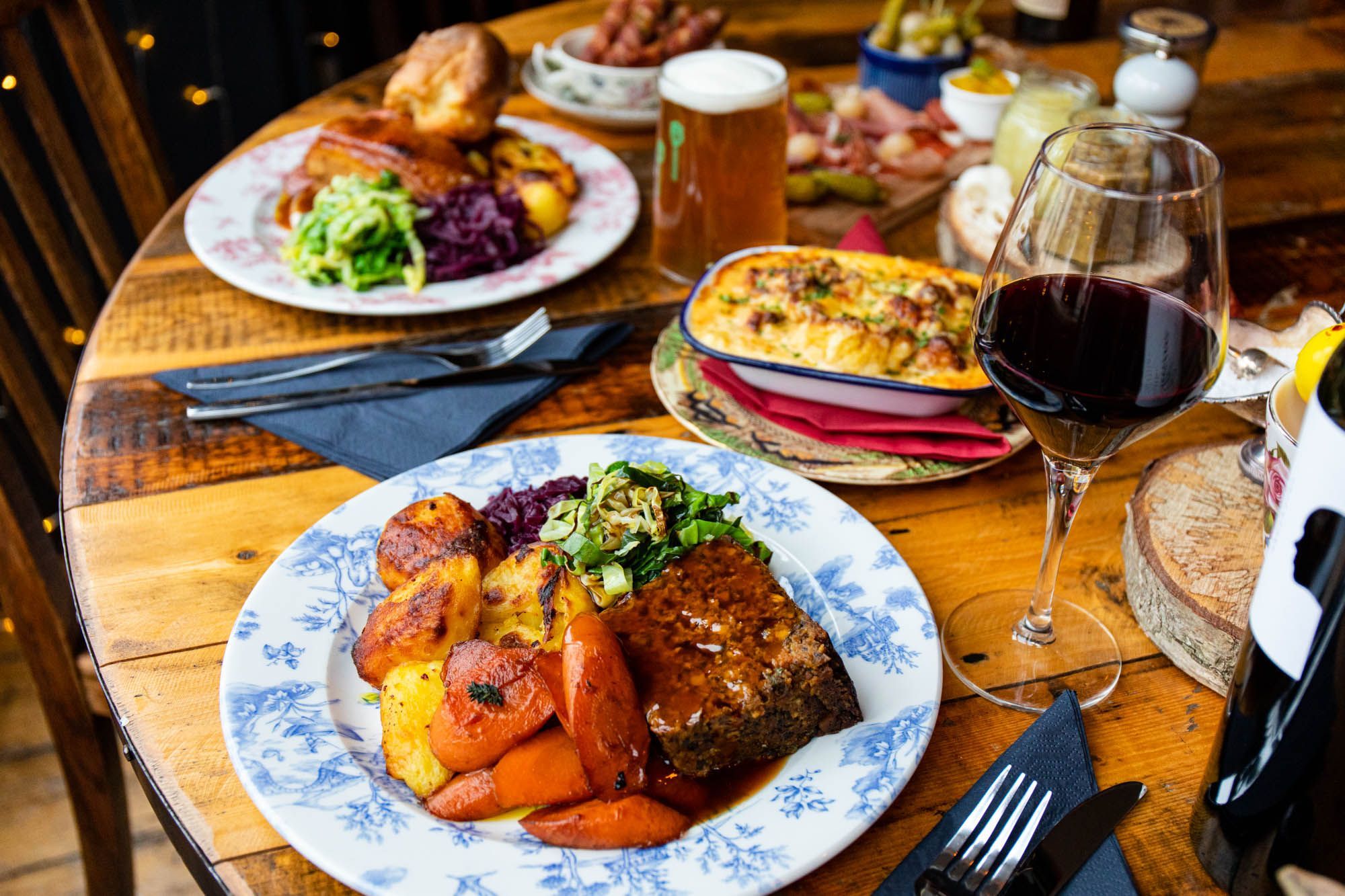 close up shot of the Sunday lunch at The Farm Tavern served on wooden table, with glass of beer and glass of red wine