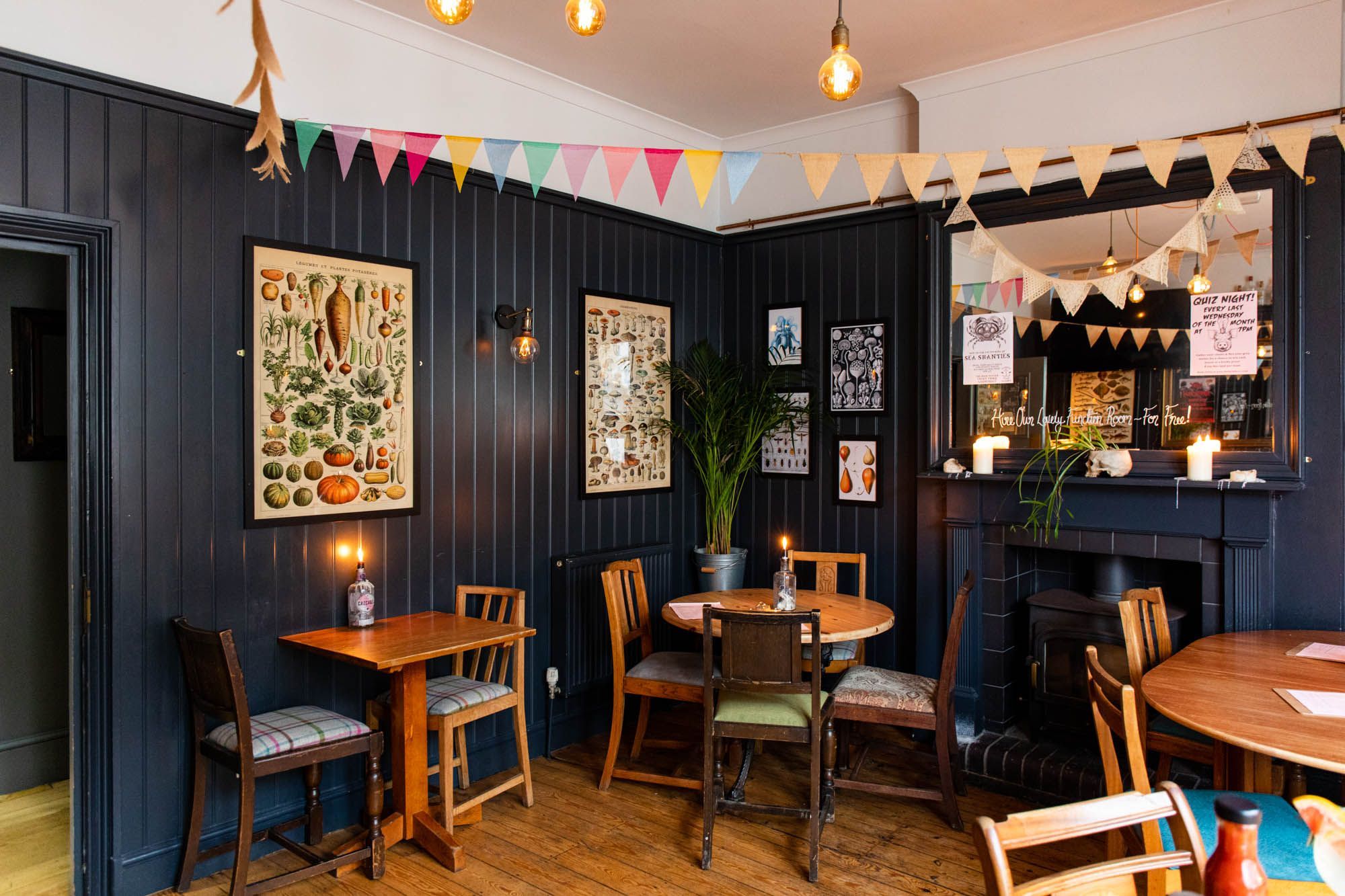 interior shot of The Farm Tavern Hove, dark blue wooden walls, pictures on the wall, brown chairs and brown tables, dim lights and decoration on ceiling