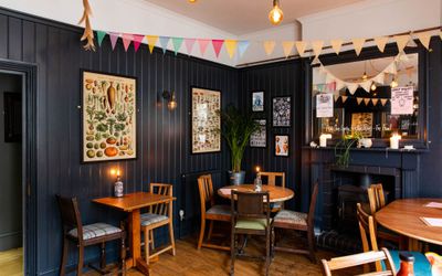 interior shot of The Farm Tavern Hove, dark blue wooden walls, pictures on the wall, brown chairs and brown tables, dim lights and decoration on ceiling